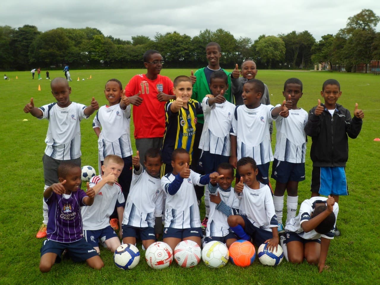 A BSCA junior football team and coaches giving thumbs up on a playing field in Bolton